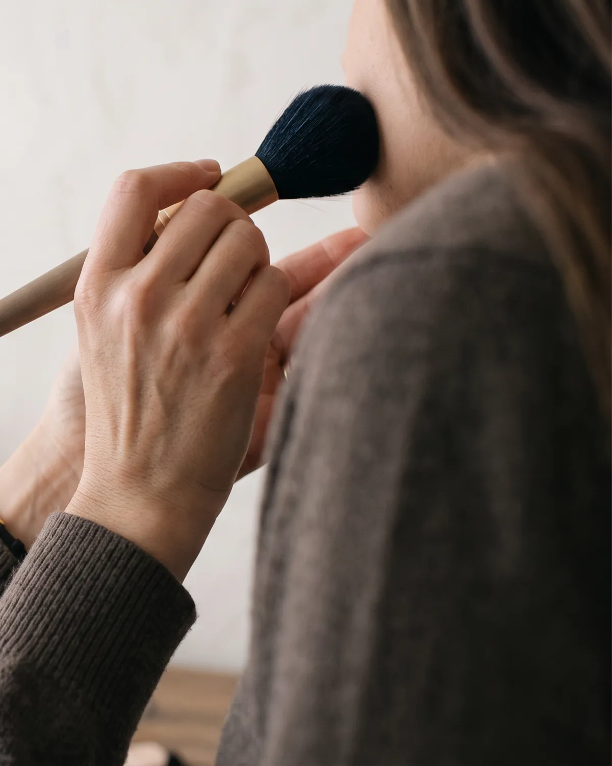 Visagistin trägt mit einem Puderpinsel Make-up auf